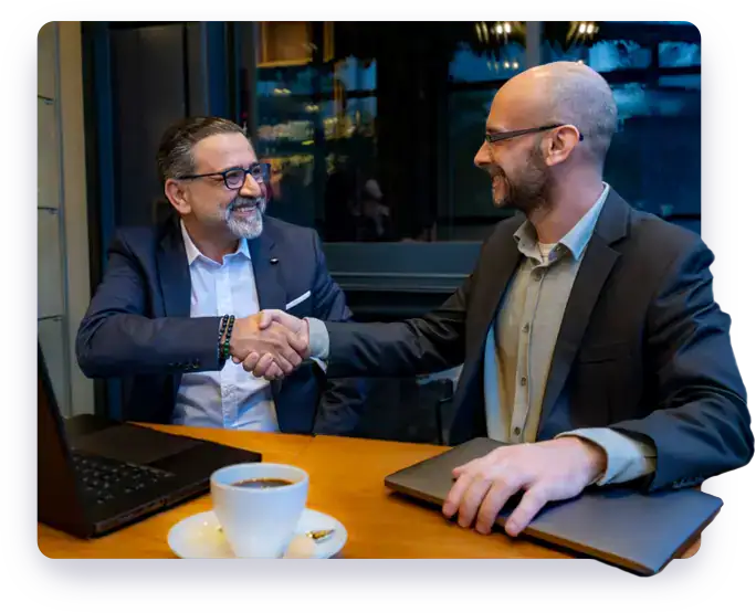 Homepage 7 Two men shaking hands at a table with a laptop.